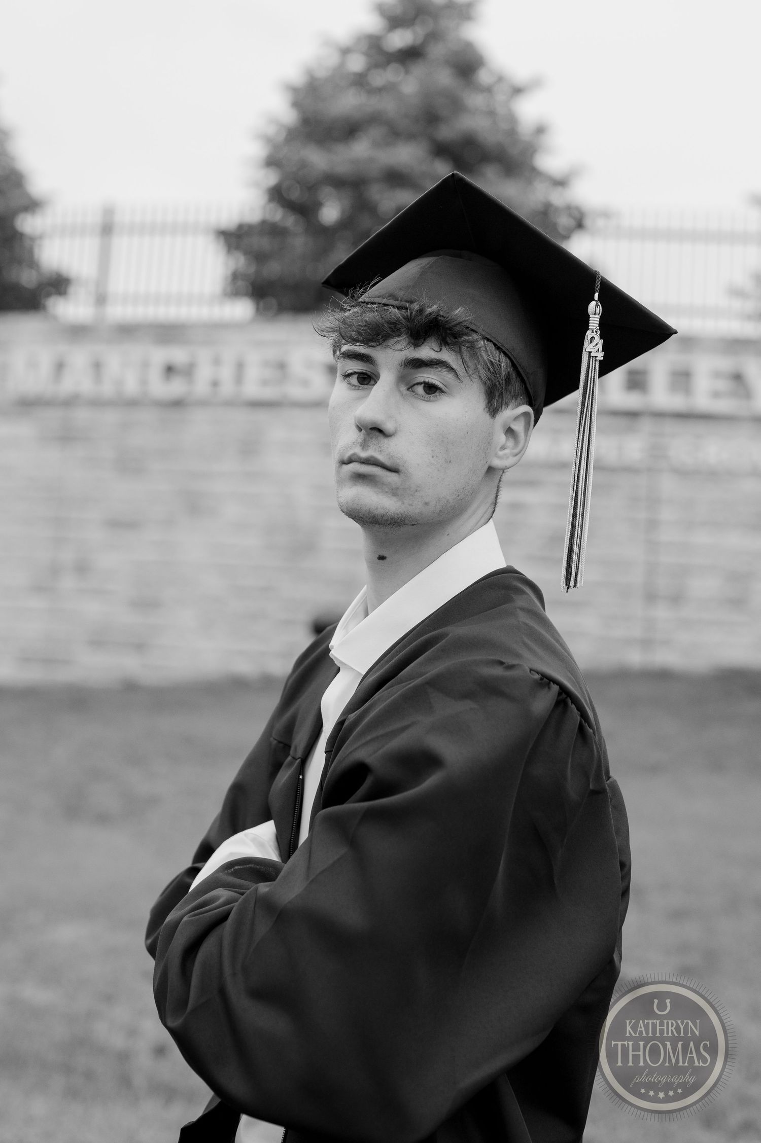 Black and white portrait of graduate in cap and gown against brick wall.