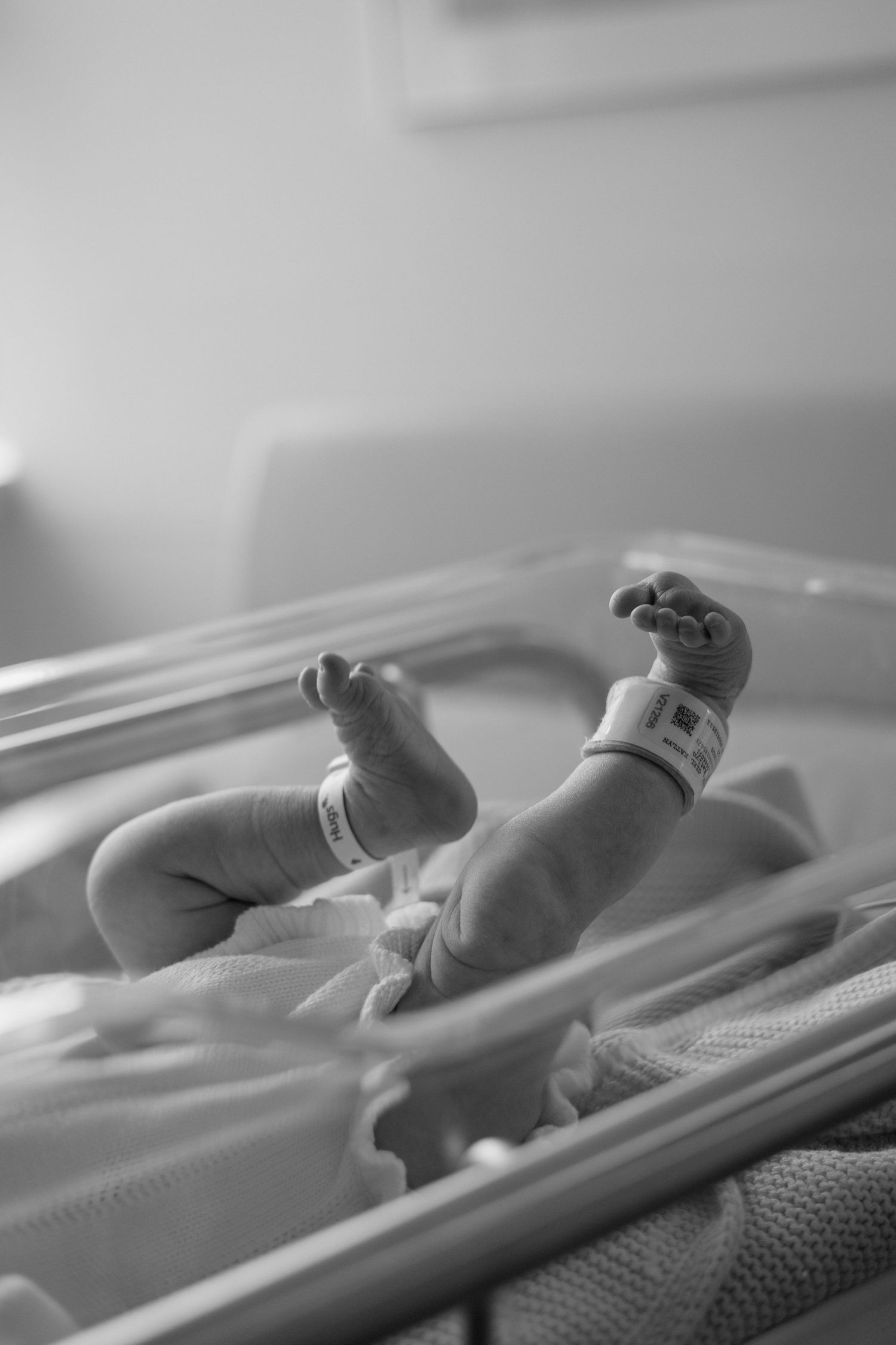 A newborn baby sleeps peacefully in a hospital bassinet under soft lighting in black and white.