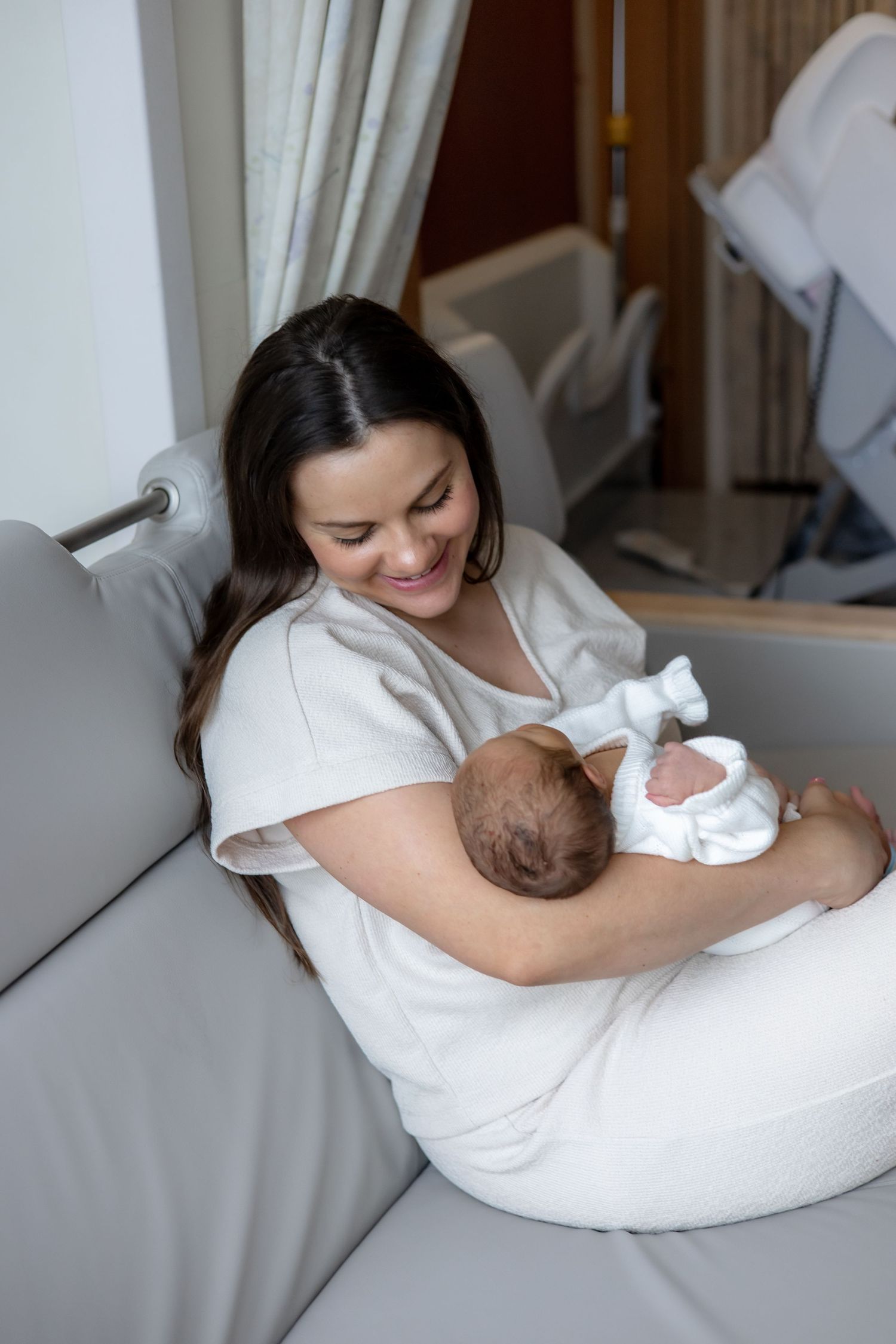 A mother and newborn share a quiet bonding moment on a white cozy nursing pillow during a breastfeeding session.