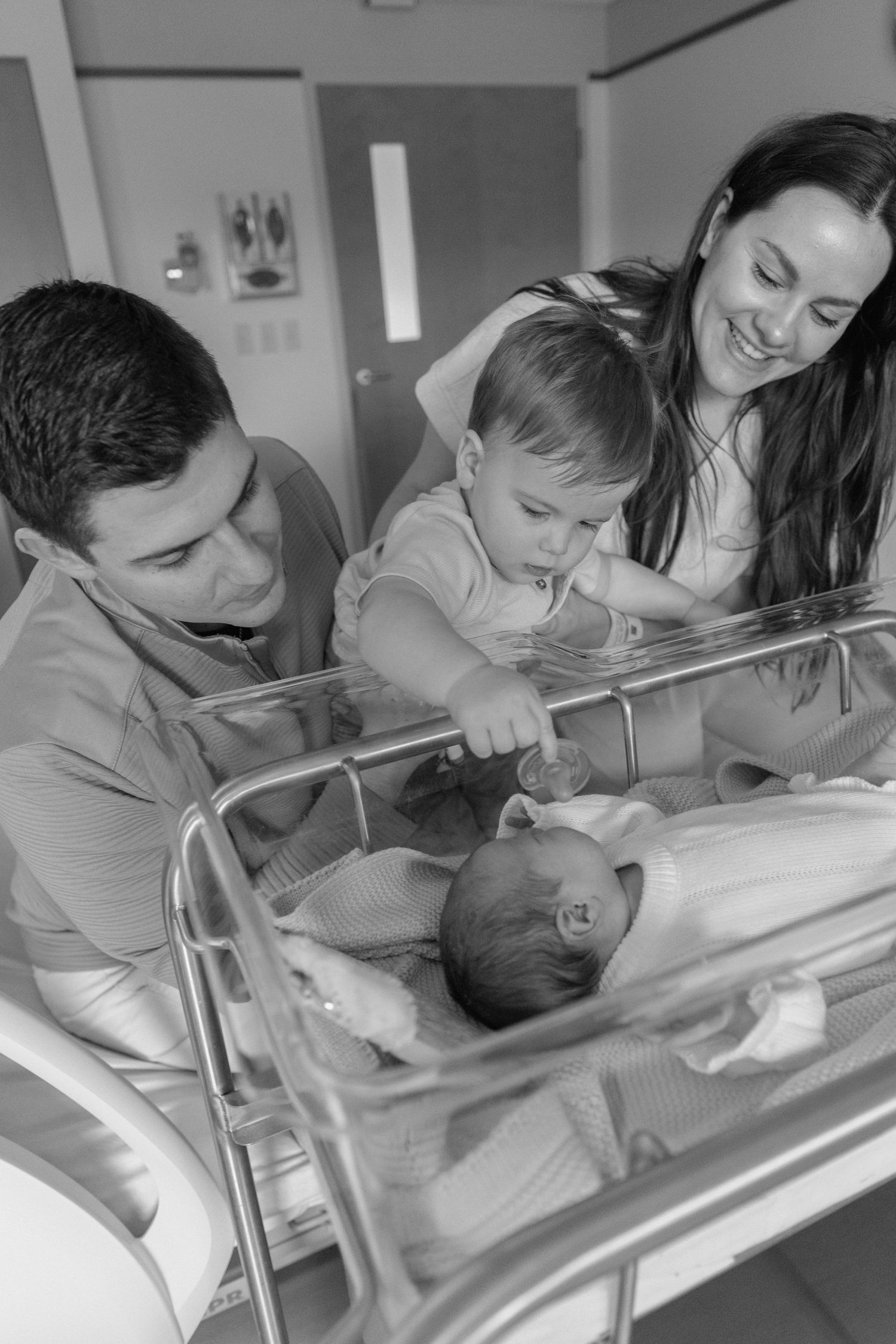 A series of black and white photos showing tender moments with a newborn baby in a hospital bassinet.