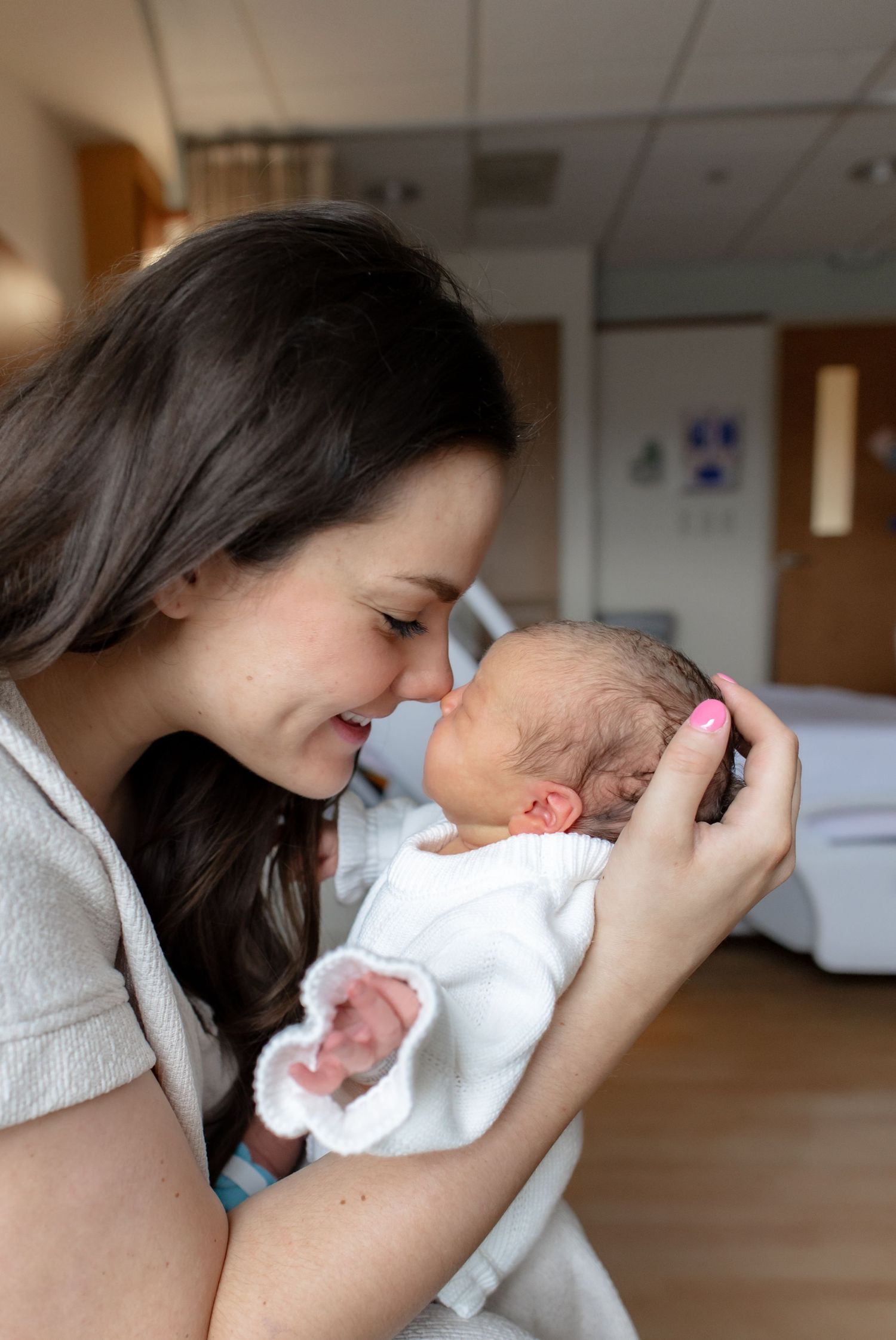 Woman leaning over and bonding with a newborn baby wrapped in a white blanket in a hospital room setting.