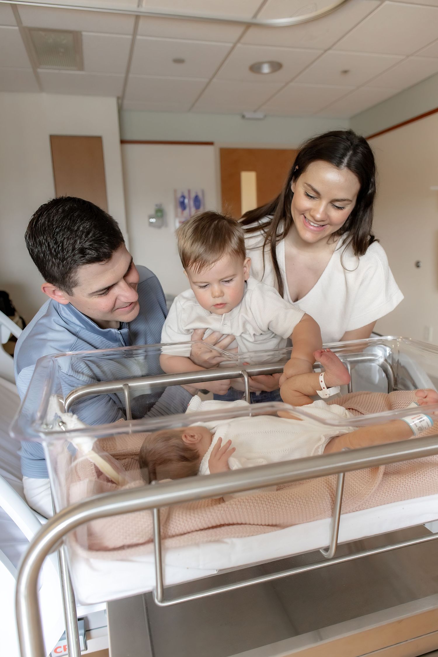 Parents gazing adoringly at their newborn baby through a hospital bassinet in a series of tender moments.