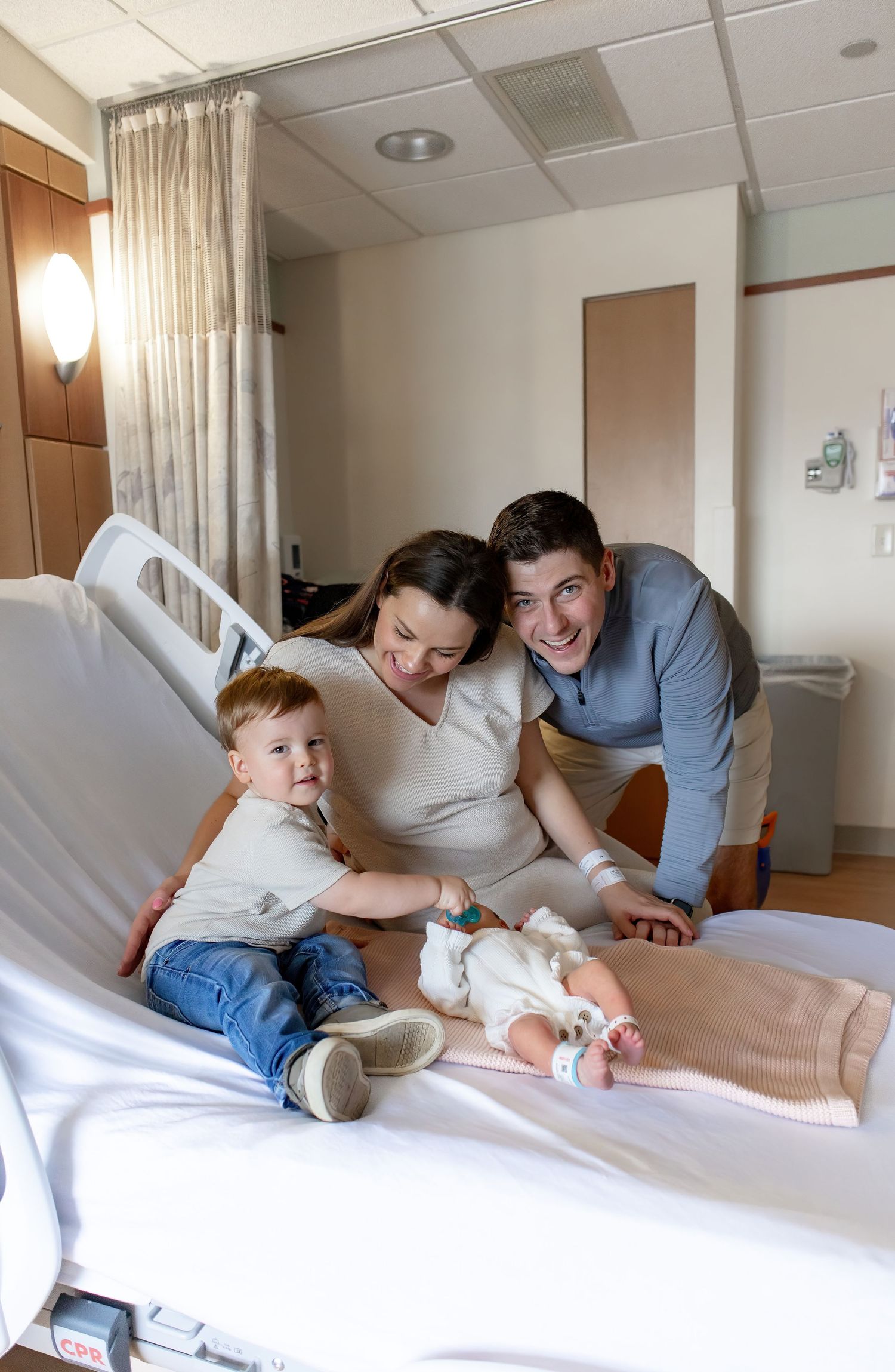 Family spending quality time together on a hospital bed while caring for their newborn baby.