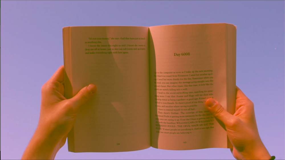Hands holding open a book against a purple-tinted background.