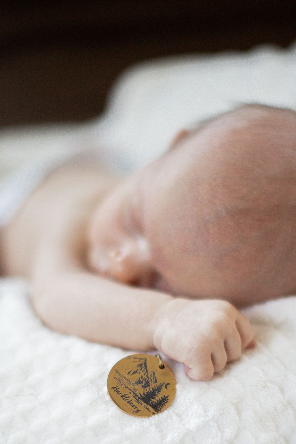 Sleeping infant's hand gently holds a medallion on white bedding.