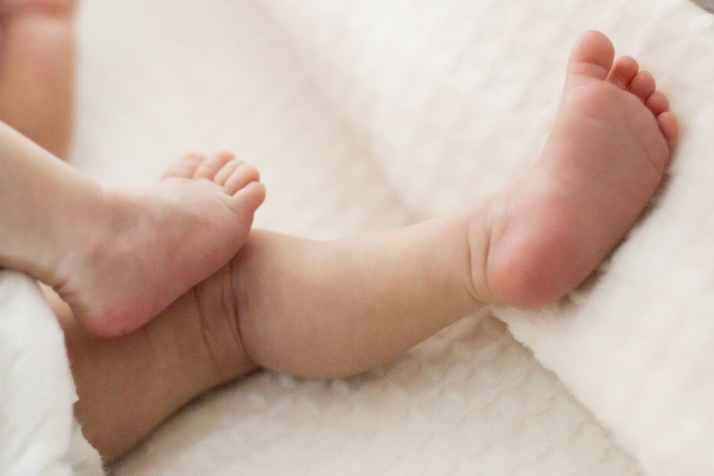 Small baby feet and legs laying on soft white fabric.