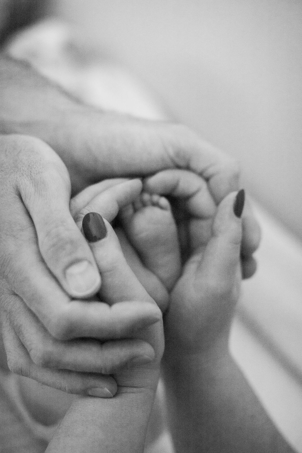 A tender black and white close-up of adult hands gently holding a baby's tiny hand with painted nails.