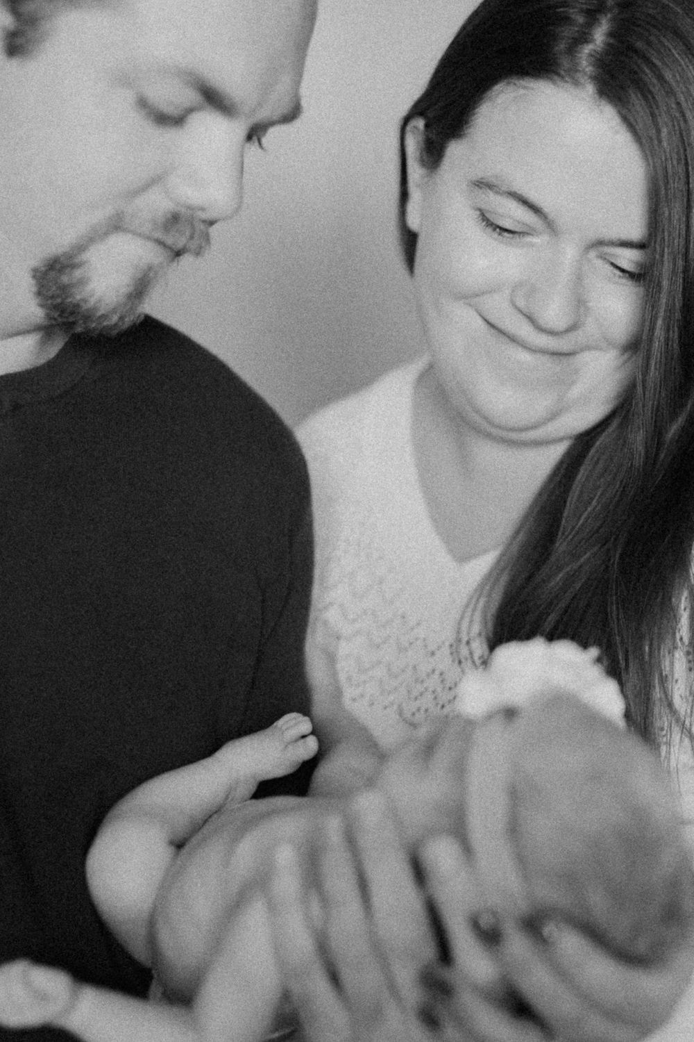 A tender black and white family photo showing parents gazing lovingly at their newborn baby in an intimate moment.
