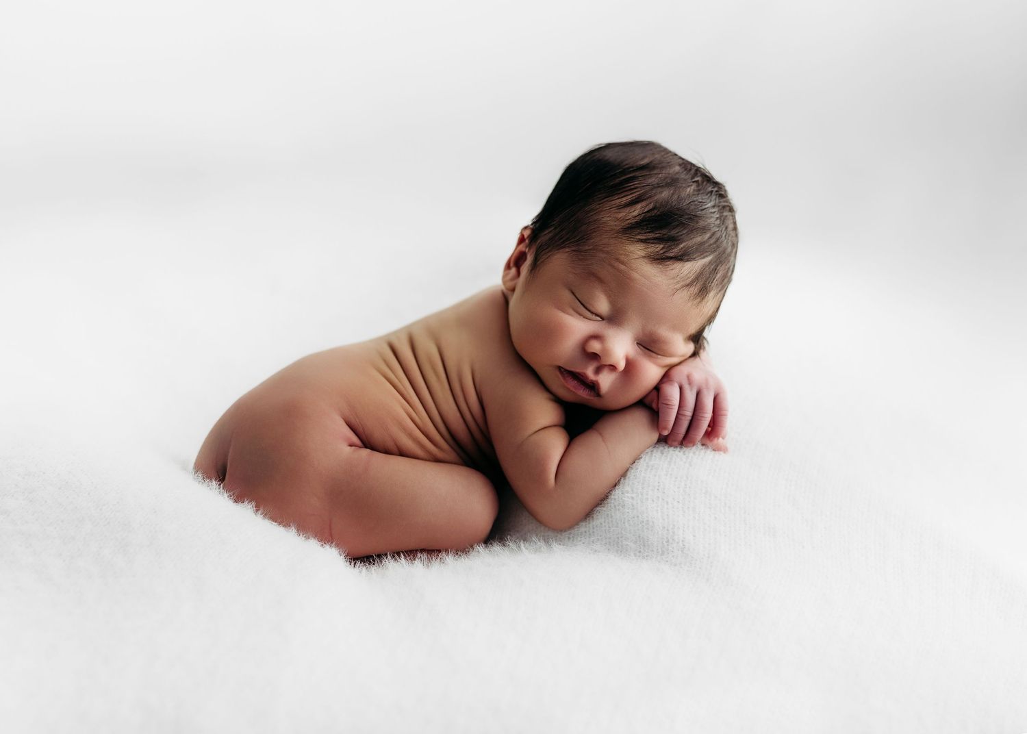 Sleeping newborn baby curled up peacefully in comfortable pose on white backdrop during professional photoshoot. Rashinphotography - Nova