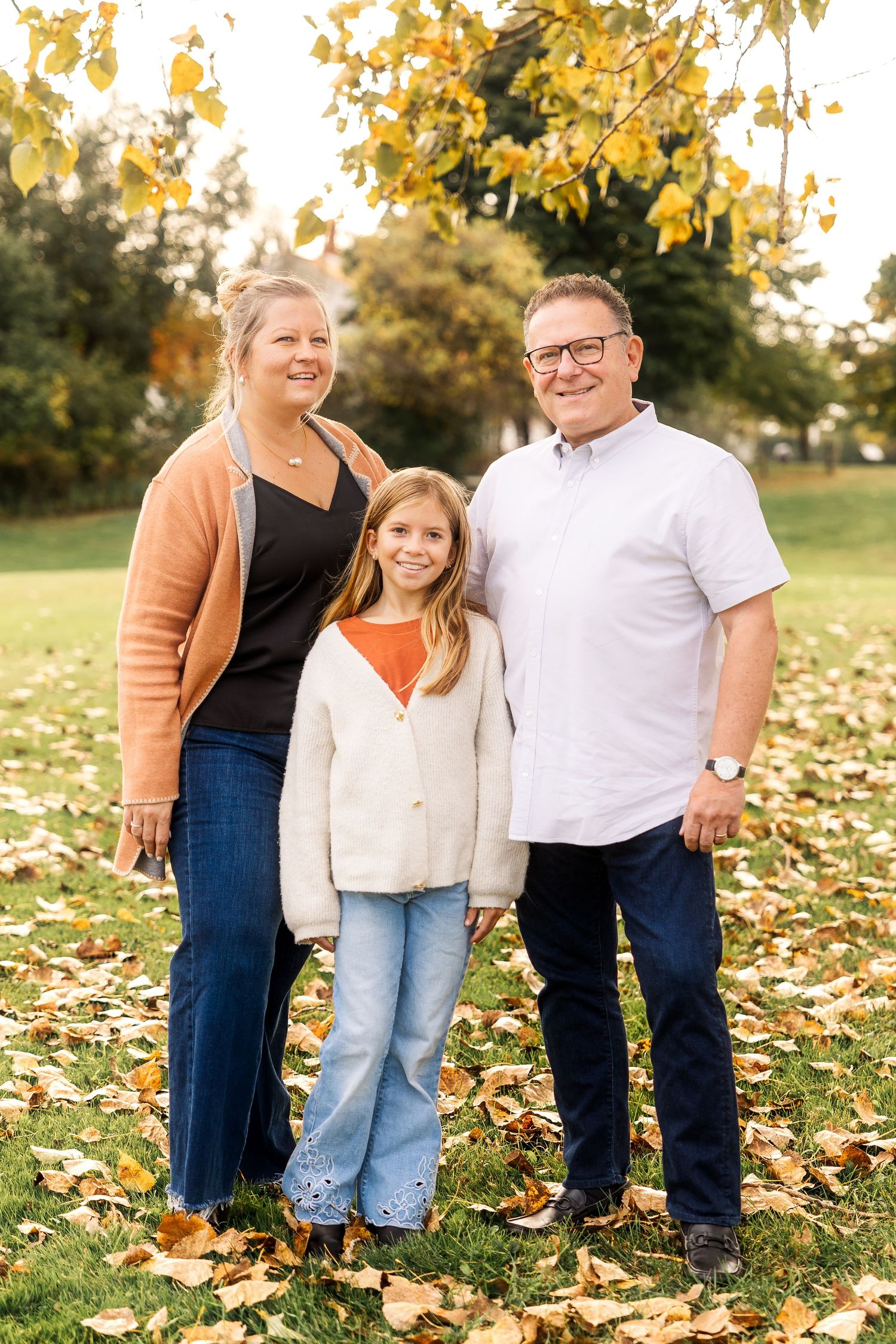 Family of three poses together on fallen autumn leaves in casual attire. Novi Northville Portrait Photographer