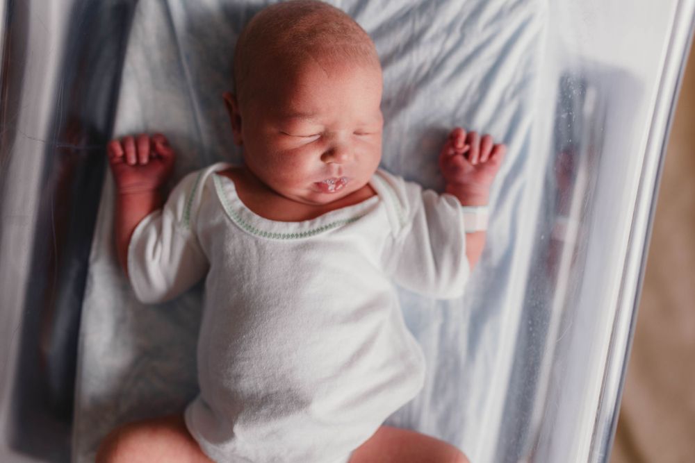 Newborn baby wearing white onesie resting on soft bedding.