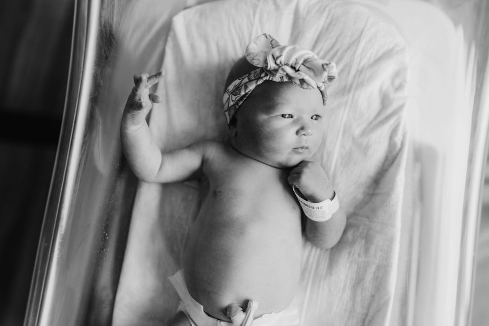 Black and white portrait of sleeping newborn wearing decorative headband.