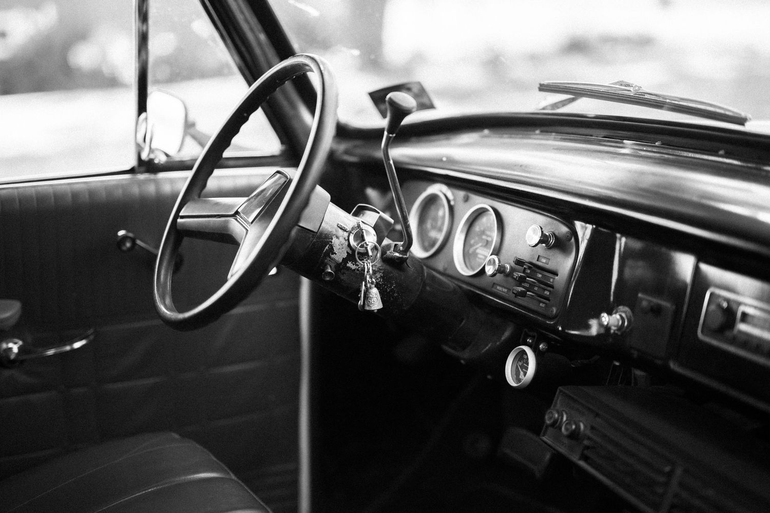 Black and white interior photo of vintage car dashboard showing steering wheel and classic gauges.