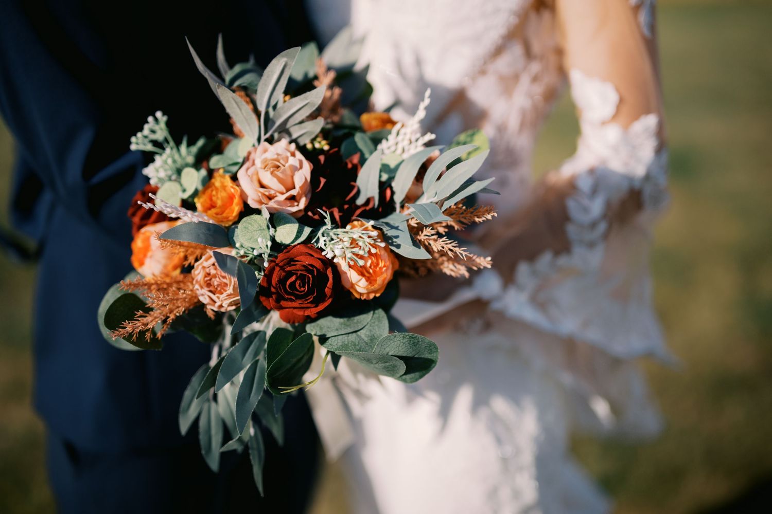 A stunning wedding bouquet with peach and burgundy roses mixed with silvery sage greenery and dried elements.