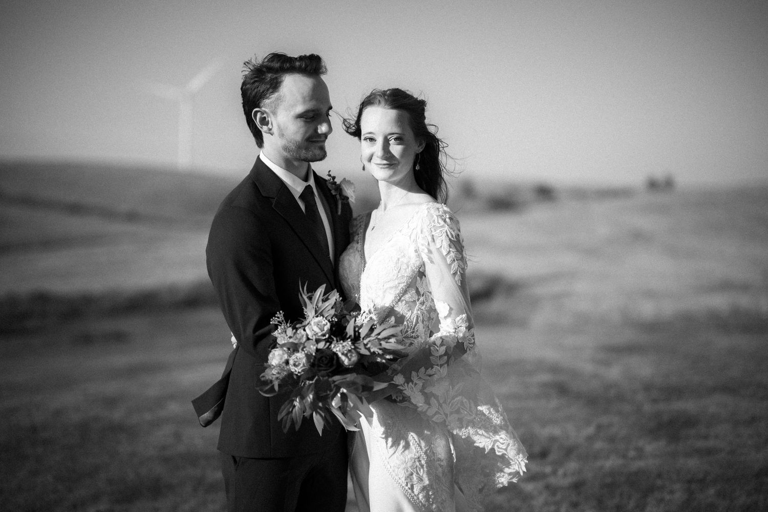 Black and white wedding portrait of newlyweds embracing in a scenic outdoor landscape with rolling hills.