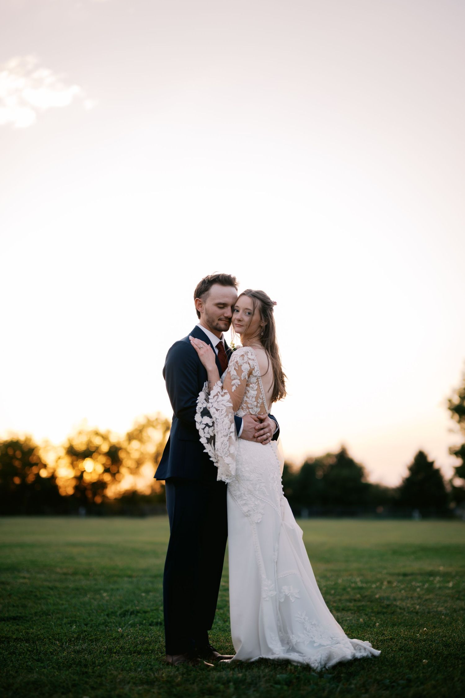 A romantic wedding portrait silhouetted against a sunset sky on a lush green lawn at dusk.