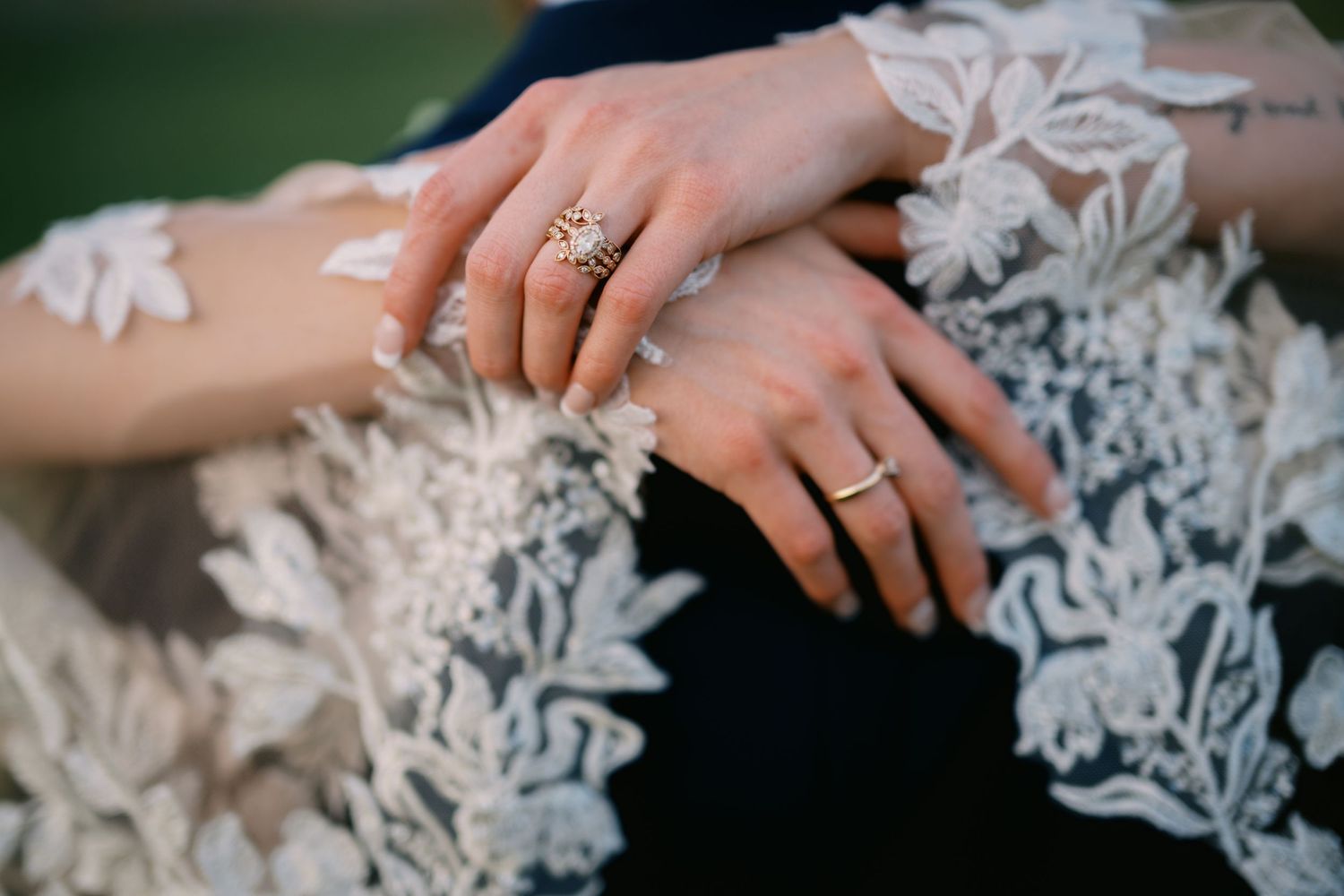 Close-up shot of hands wearing wedding rings resting on delicate white lace fabric, showing intricate bridal details.