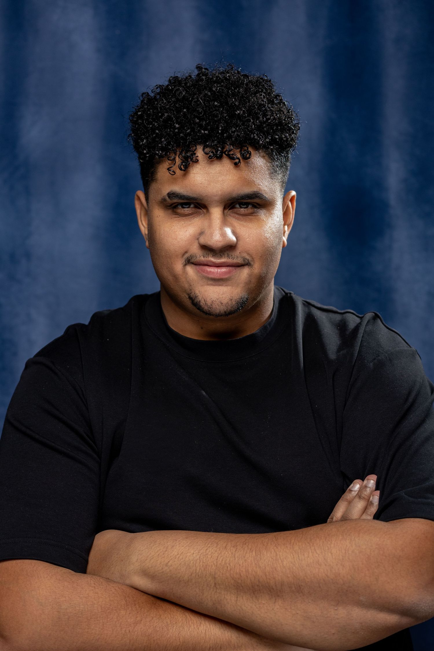 Professional portrait against a dark blue background with crossed arms.