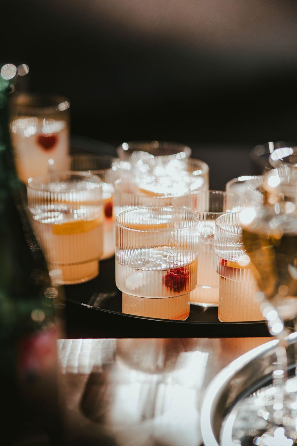 Elegant cocktails with garnishes arranged on serving tray with ice and pink-hued drinks.