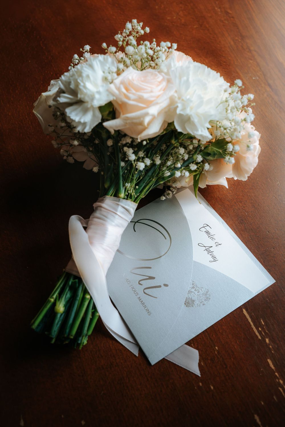Elegant wedding bouquet of white roses and baby's breath with satin ribbon beside a wedding program on wood table.
