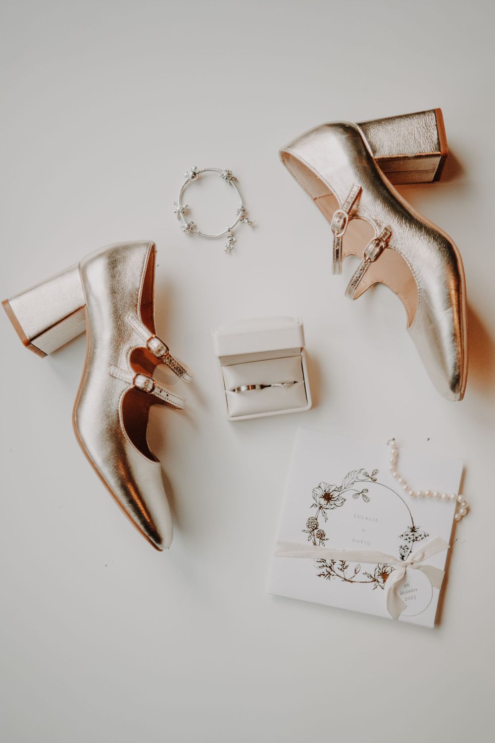 Elegant nude-colored wedding heels and invitations arranged artistically on white background.