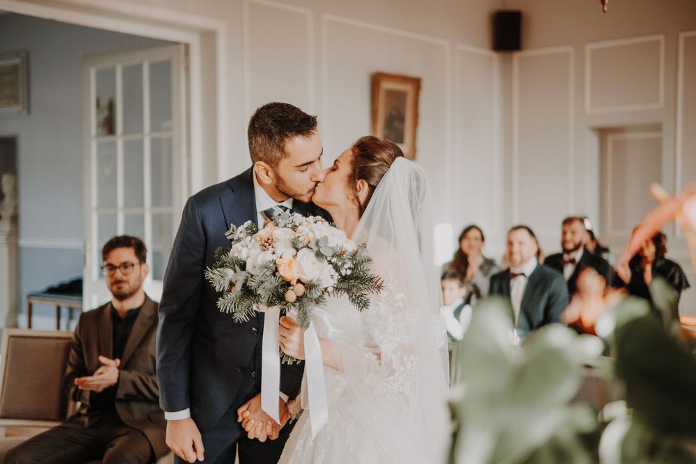 A romantic wedding couple shares an intimate kiss during their celebration while guests look on in the background.