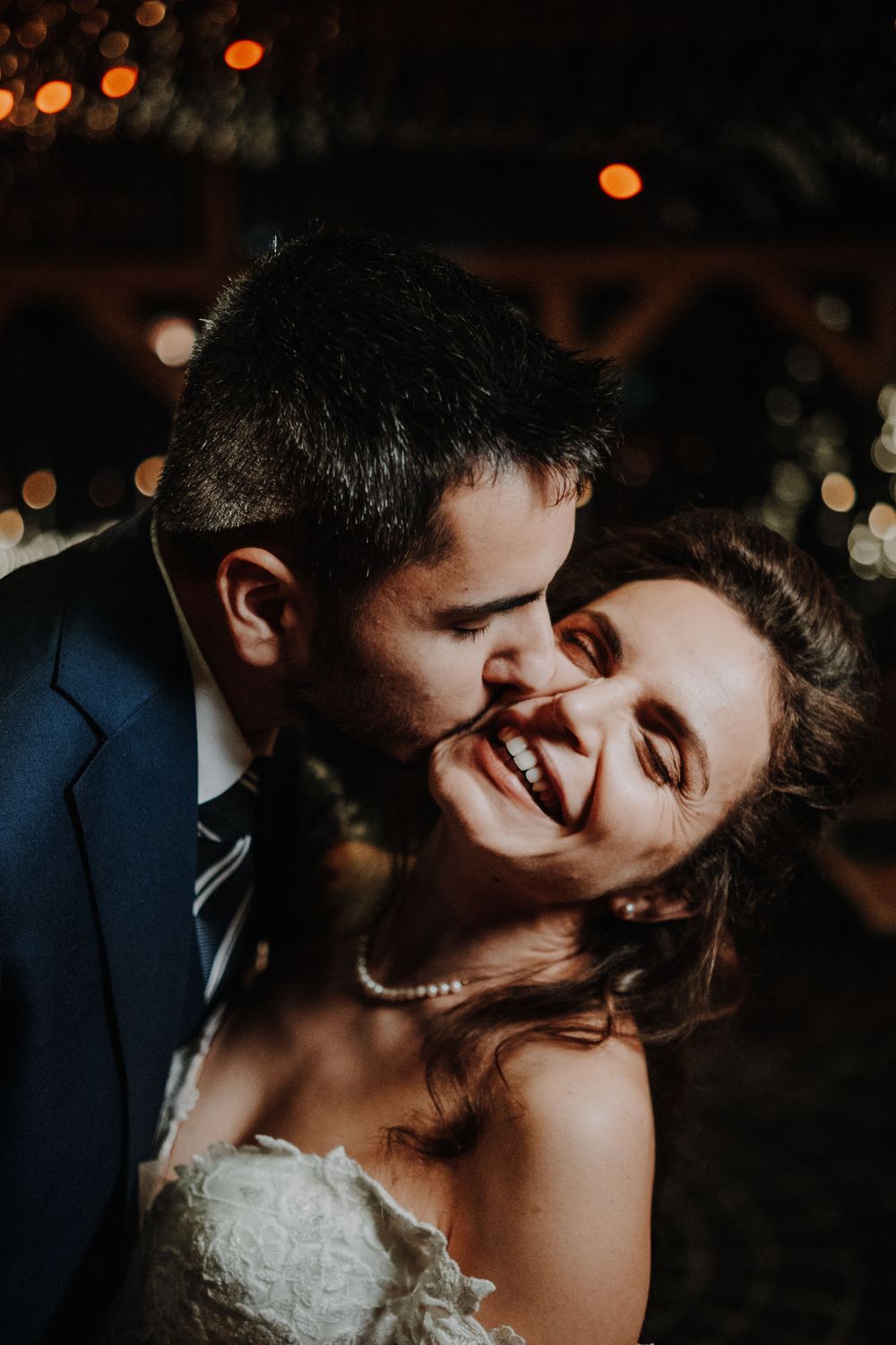 A romantic wedding couple shares an intimate kiss under warm glowing lights at their evening reception.