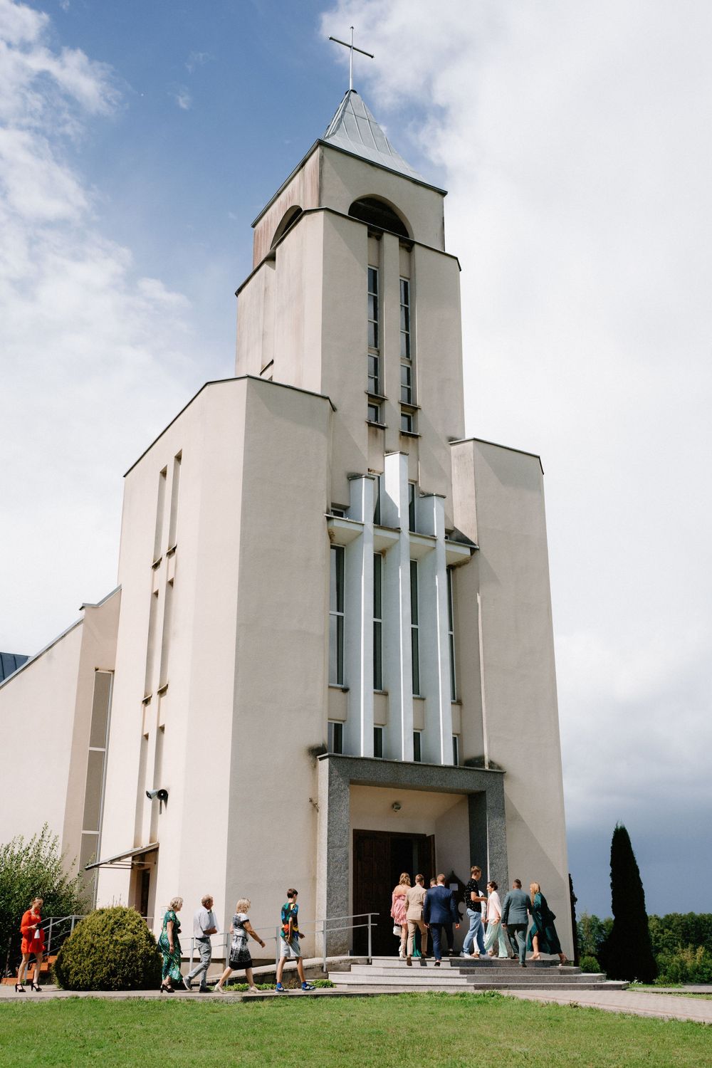 Modern white church exterior with angular architecture and bell tower against cloudy sky.