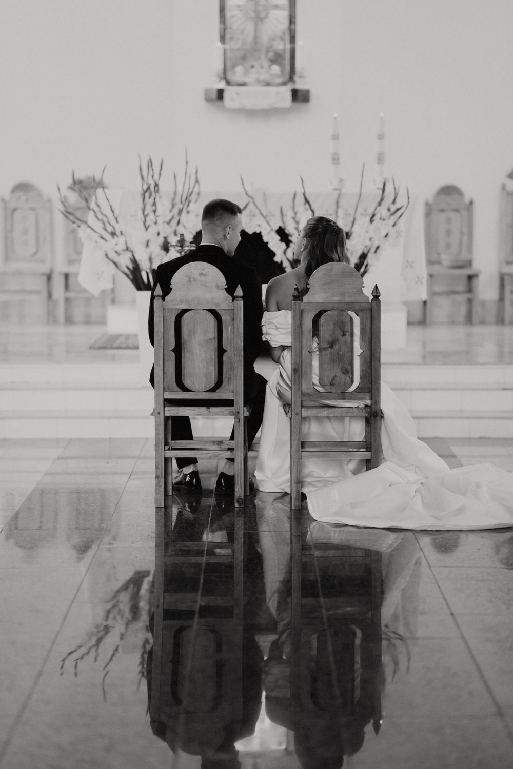 Artistic black and white reflection of ornate church chairs on polished floor.