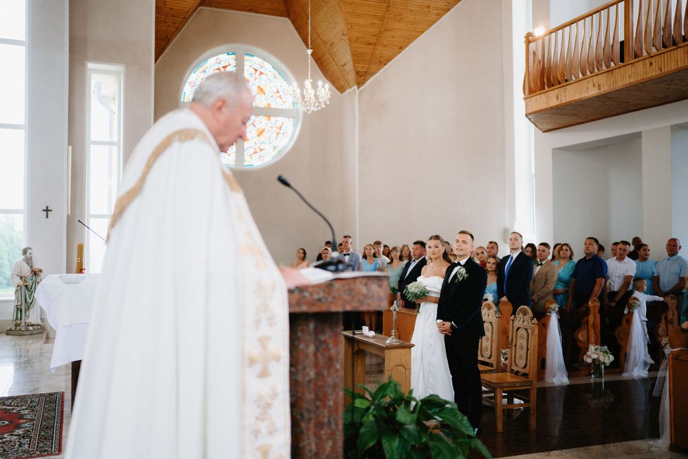 Church wedding ceremony in progress with wooden ceiling beams and natural lighting.