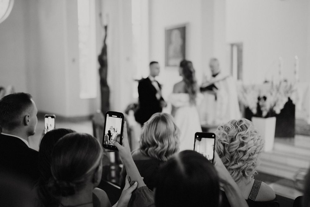 Wedding guests capturing ceremony moments on smartphones in church.