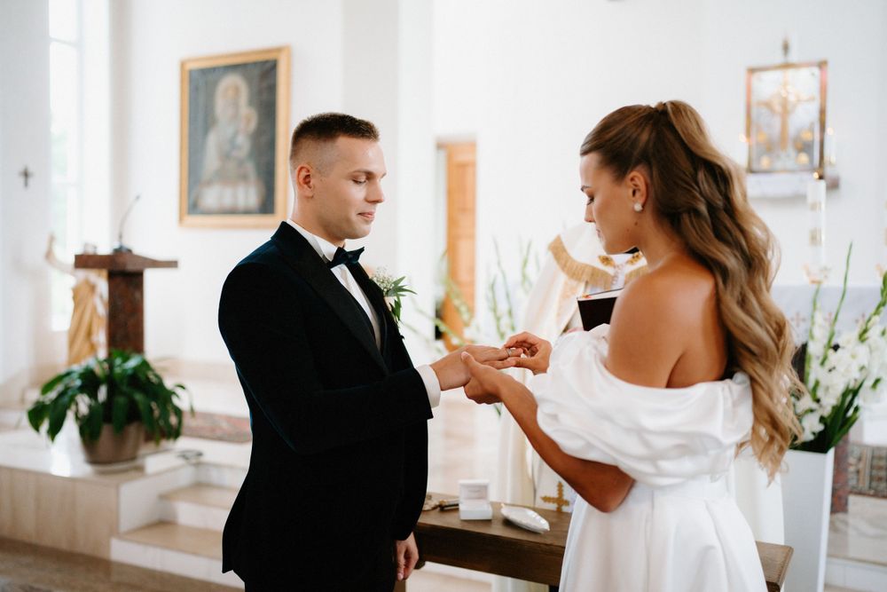 Elegant church wedding ceremony with guests seated in white pews and natural light streaming through windows.