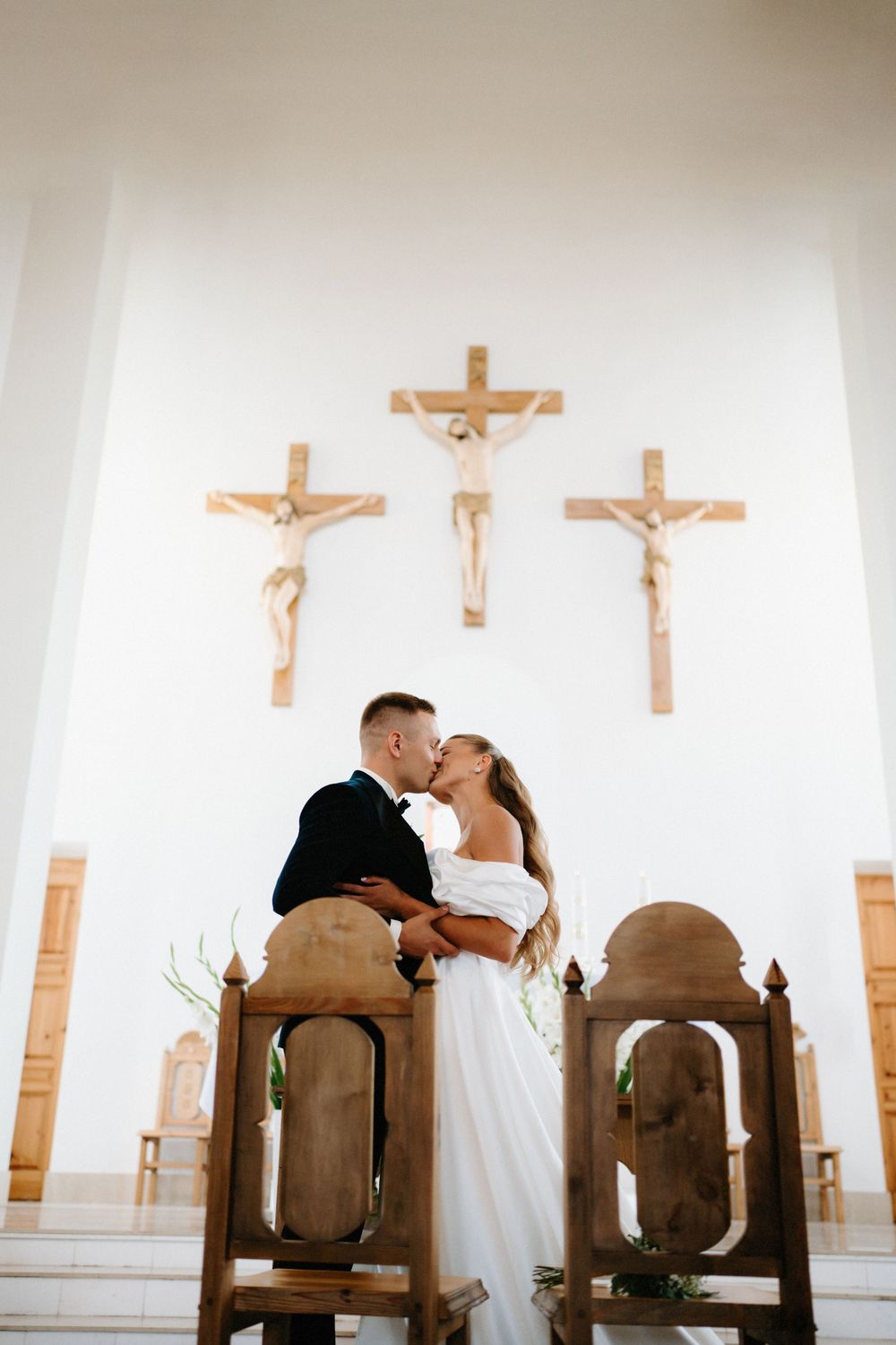 Intimate church wedding scene with crucifixes mounted on white walls.