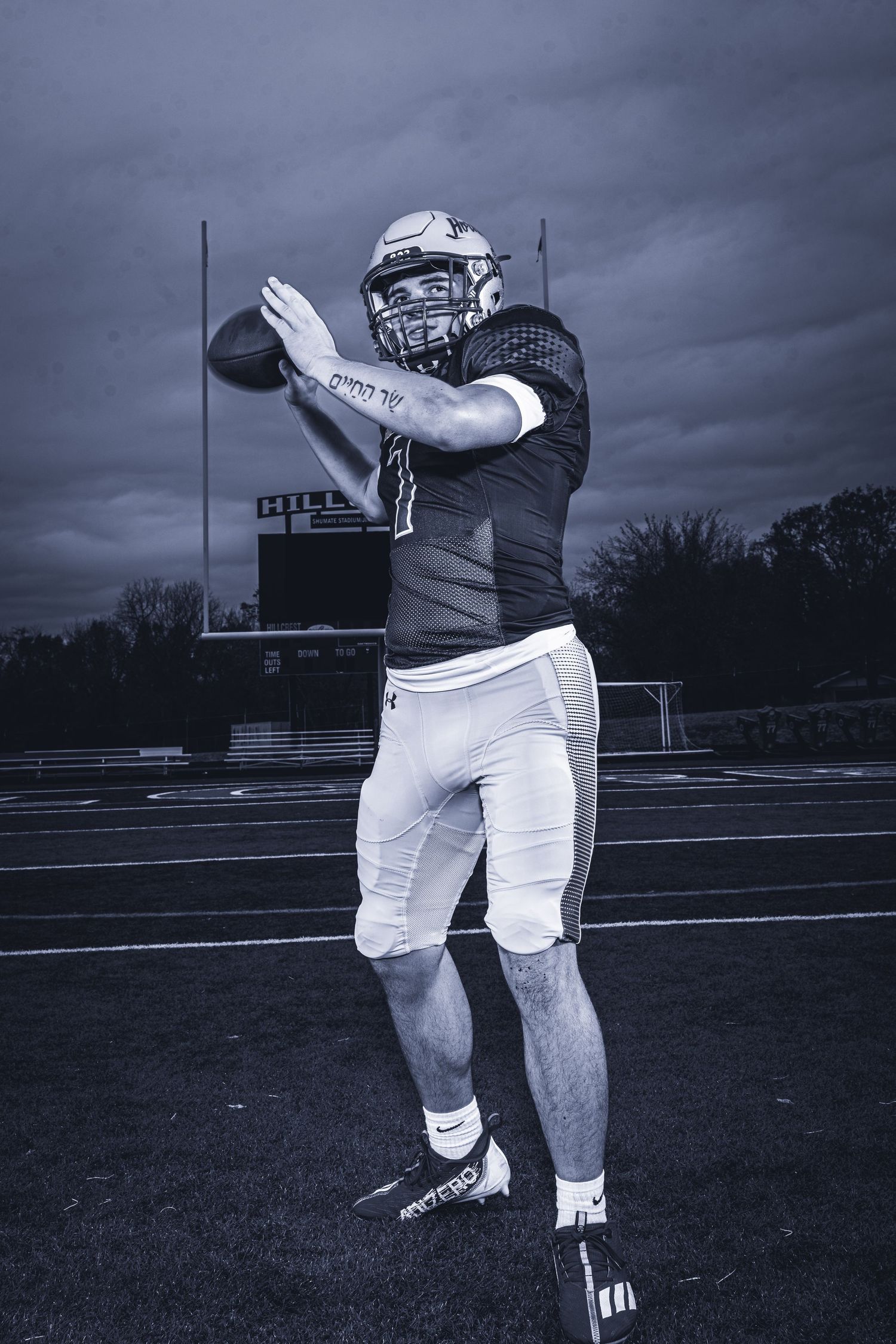Football player throwing ball on field against stormy sky in monochrome.
