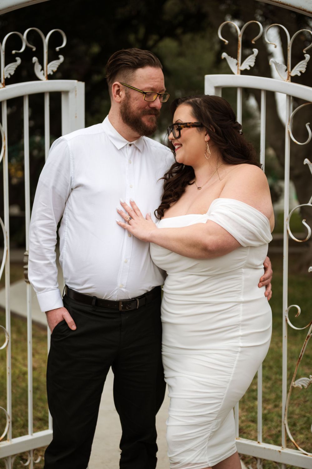 Joyful couple sharing intimate moment by decorative white metal garden gate.