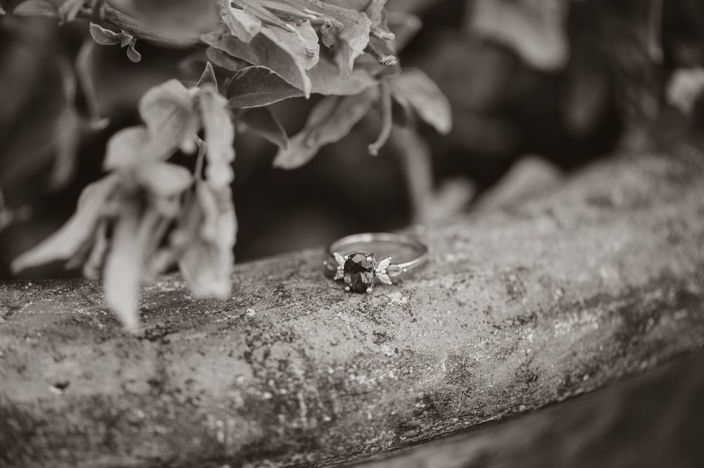 A black and white detail shot of an engagement ring on weathered wood.