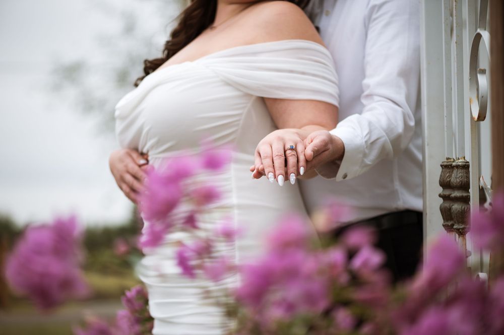 A romantic couple's portrait through pink flowers showing their wedding rings.