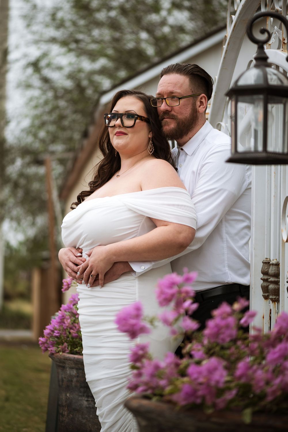 A romantic portrait of a couple embracing near a vintage lantern with pink flowers in the foreground.