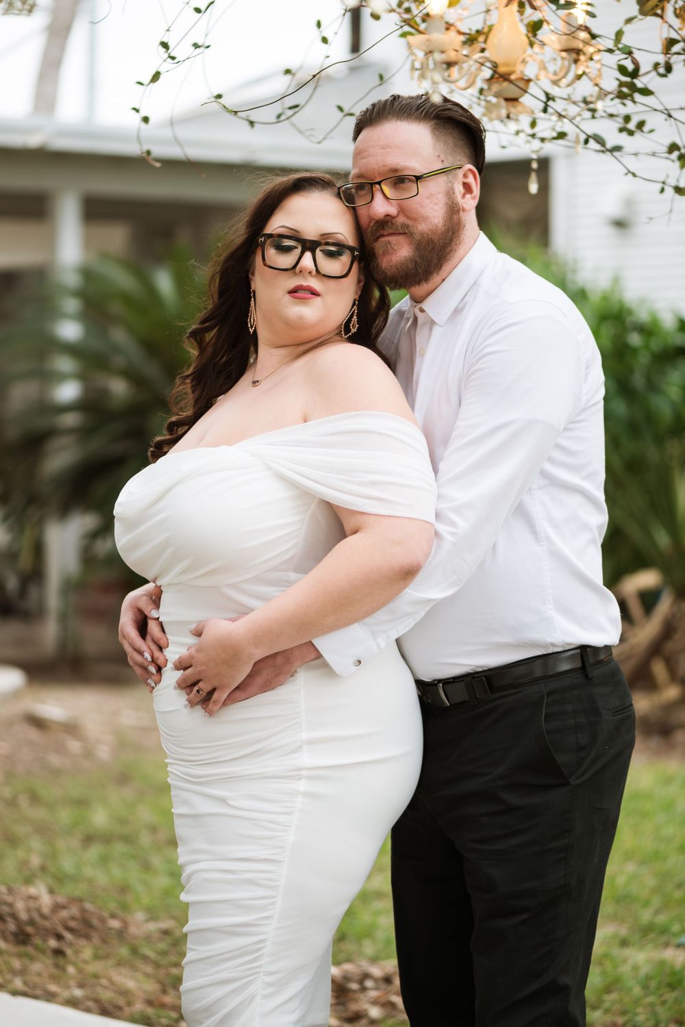 An intimate portrait of a couple in white and black attire against a garden backdrop.