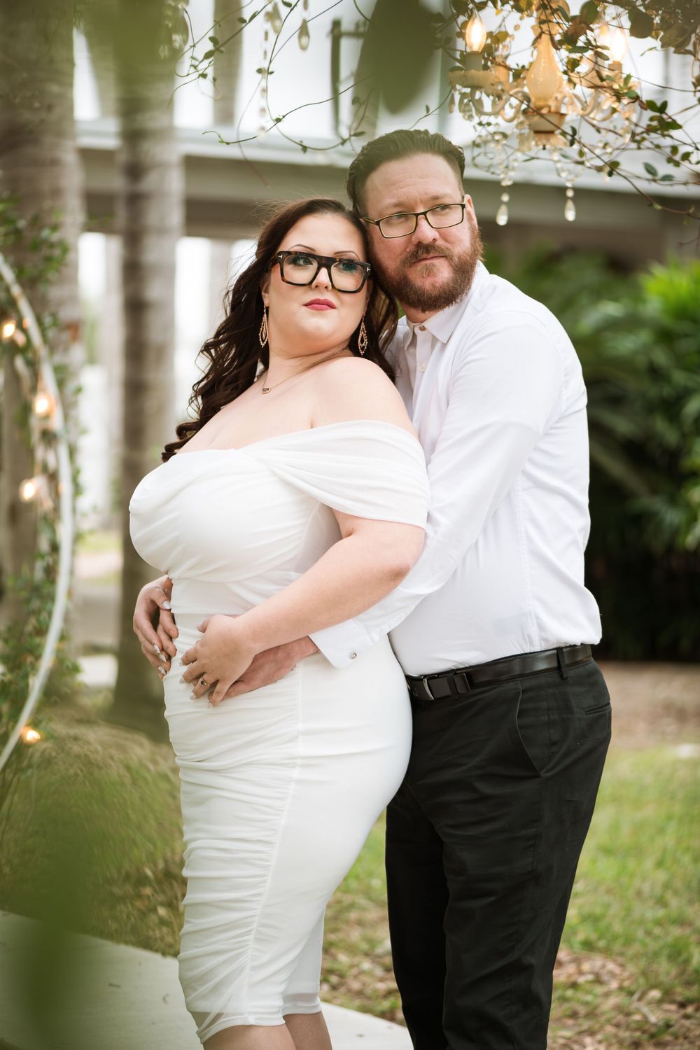 A romantic couple's portrait under twinkling lights with bride in white off-shoulder dress and groom in white shirt.
