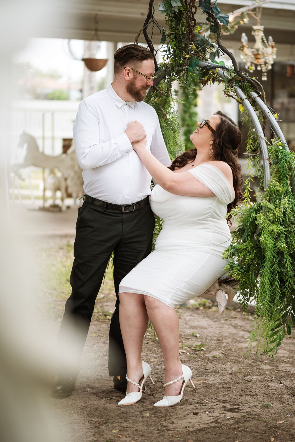 Playful wedding couple dancing and laughing under greenery in garden setting.