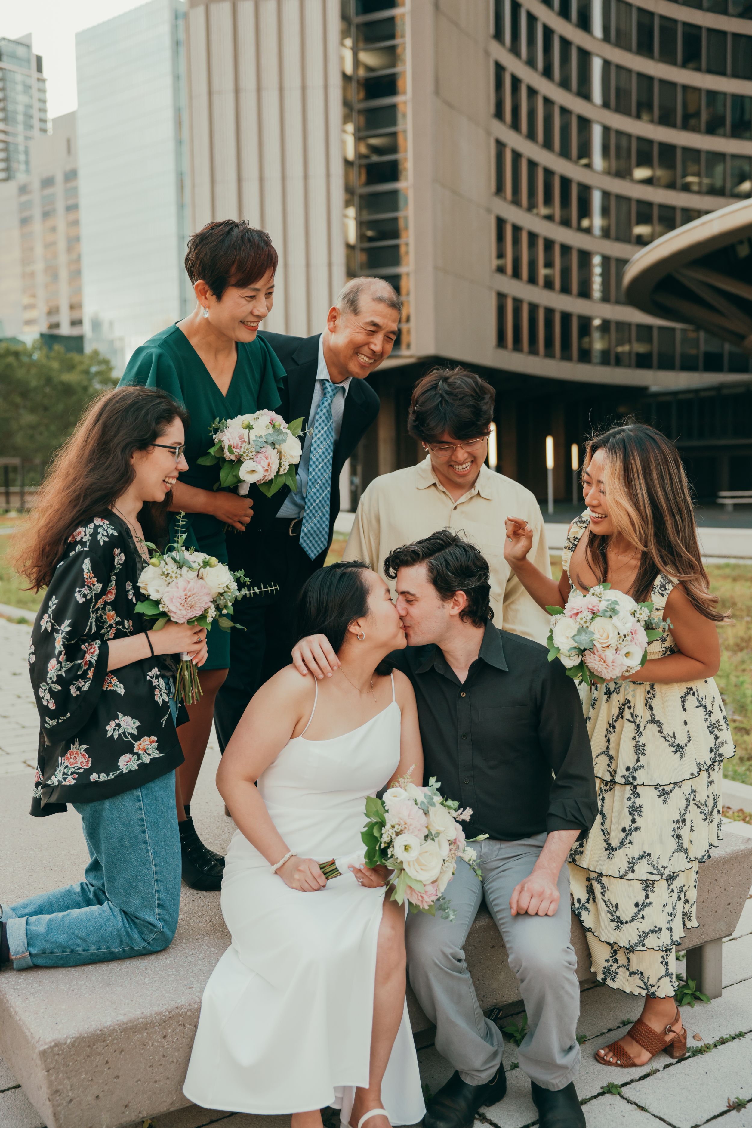 Wedding party shares joyful moment outside Toronto City Hall with bouquets.