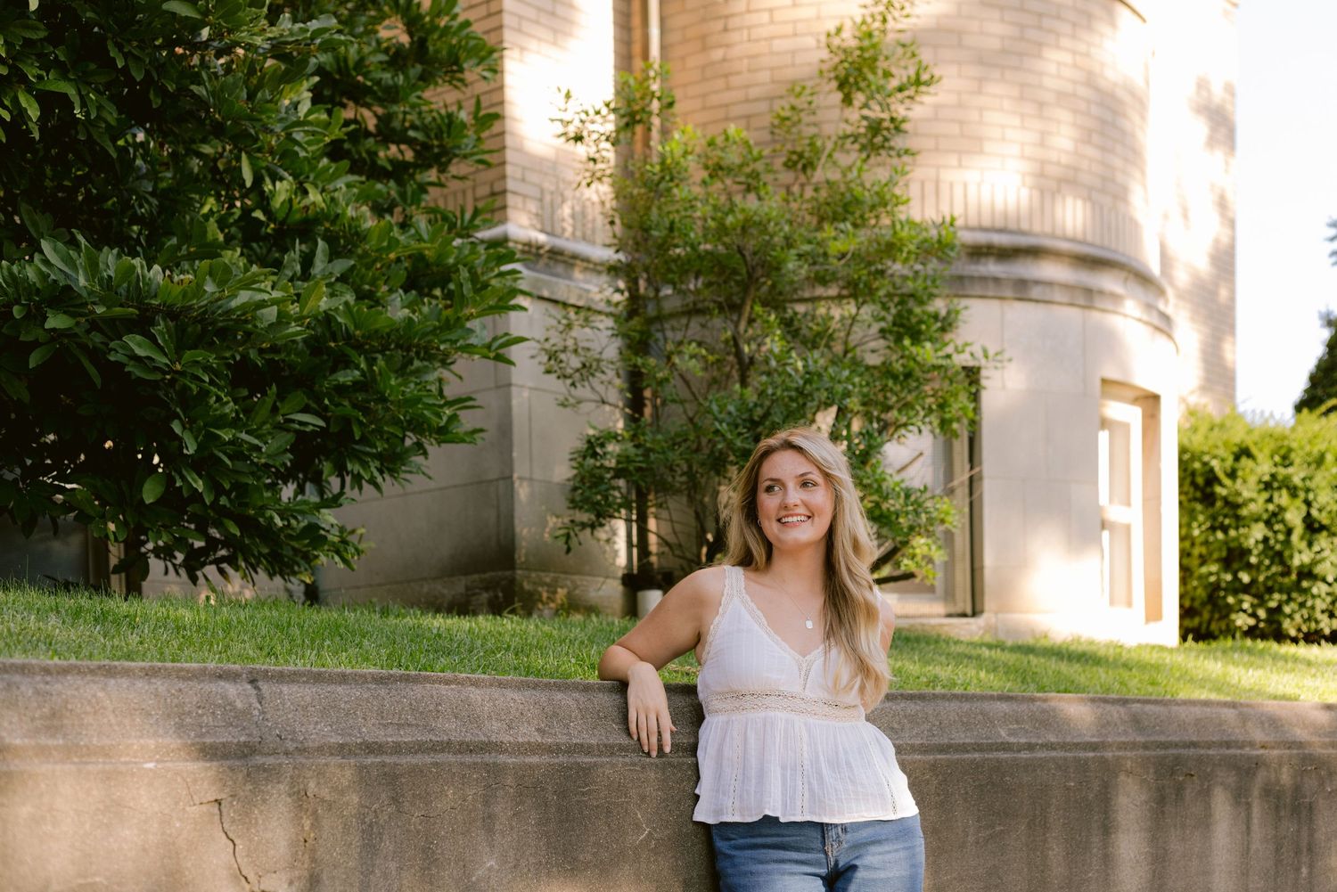 A casual summer portrait against a stone building with greenery and soft lighting.