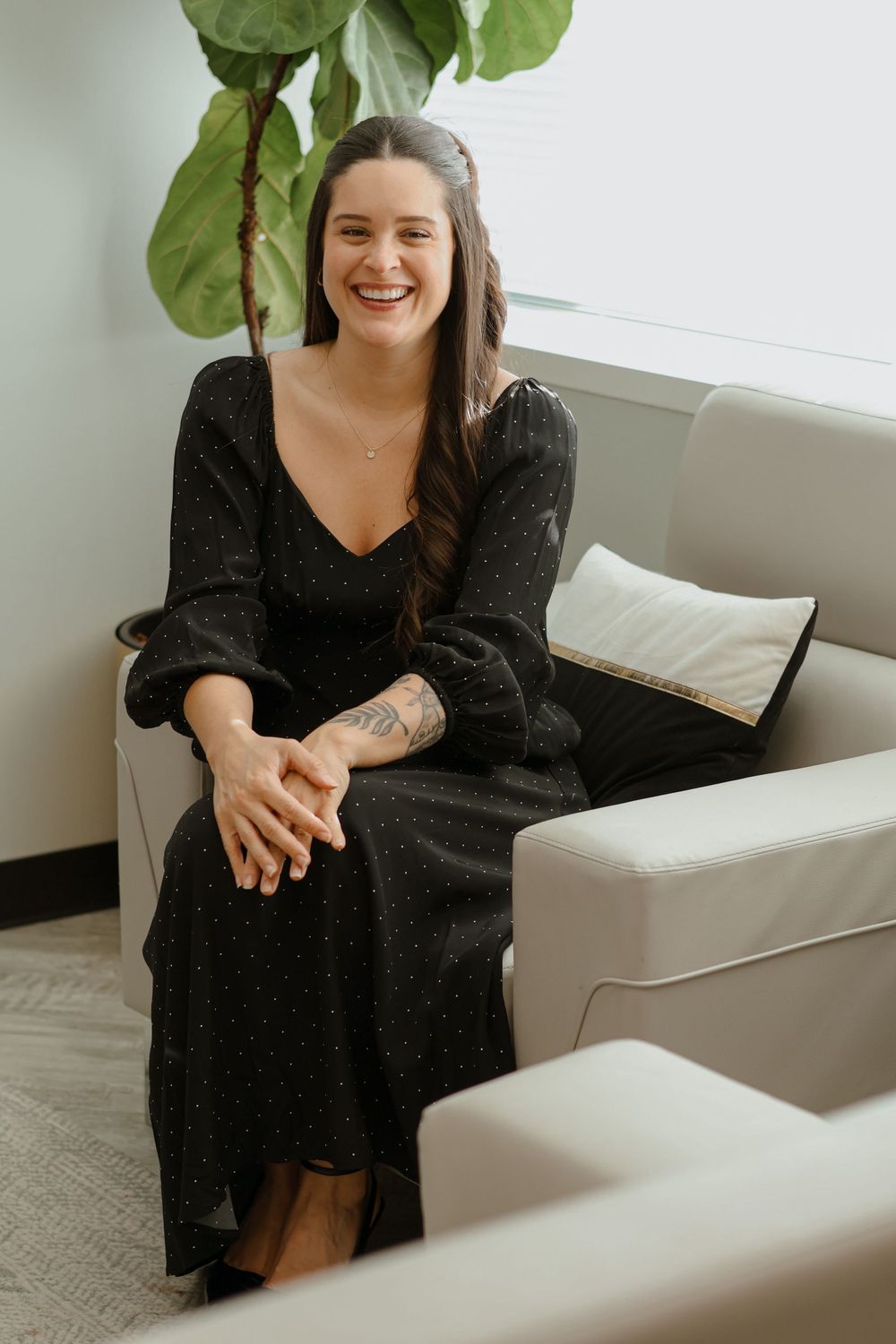 Professional sitting on a white couch in a modern office setting wearing a black dress.