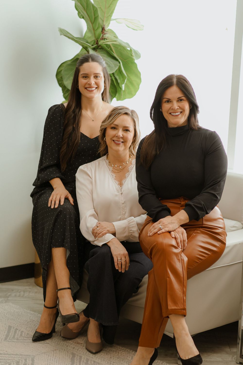 Professional lifestyle photos of women laughing on white couch with plant decor.