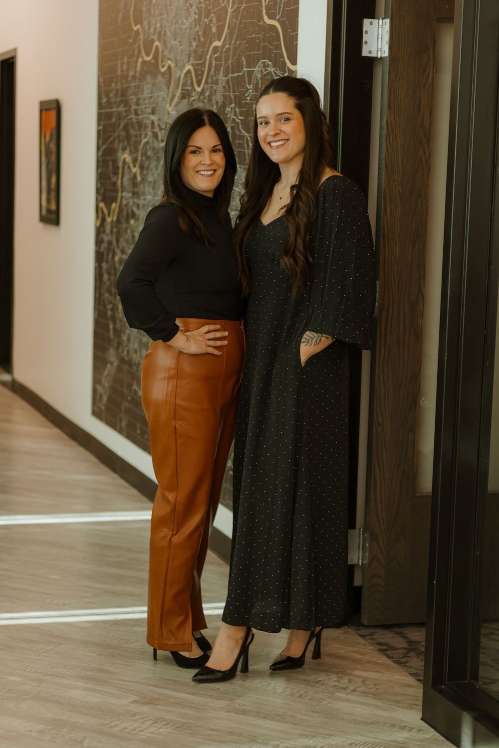 Women in business attire posing together in modern office hallway.