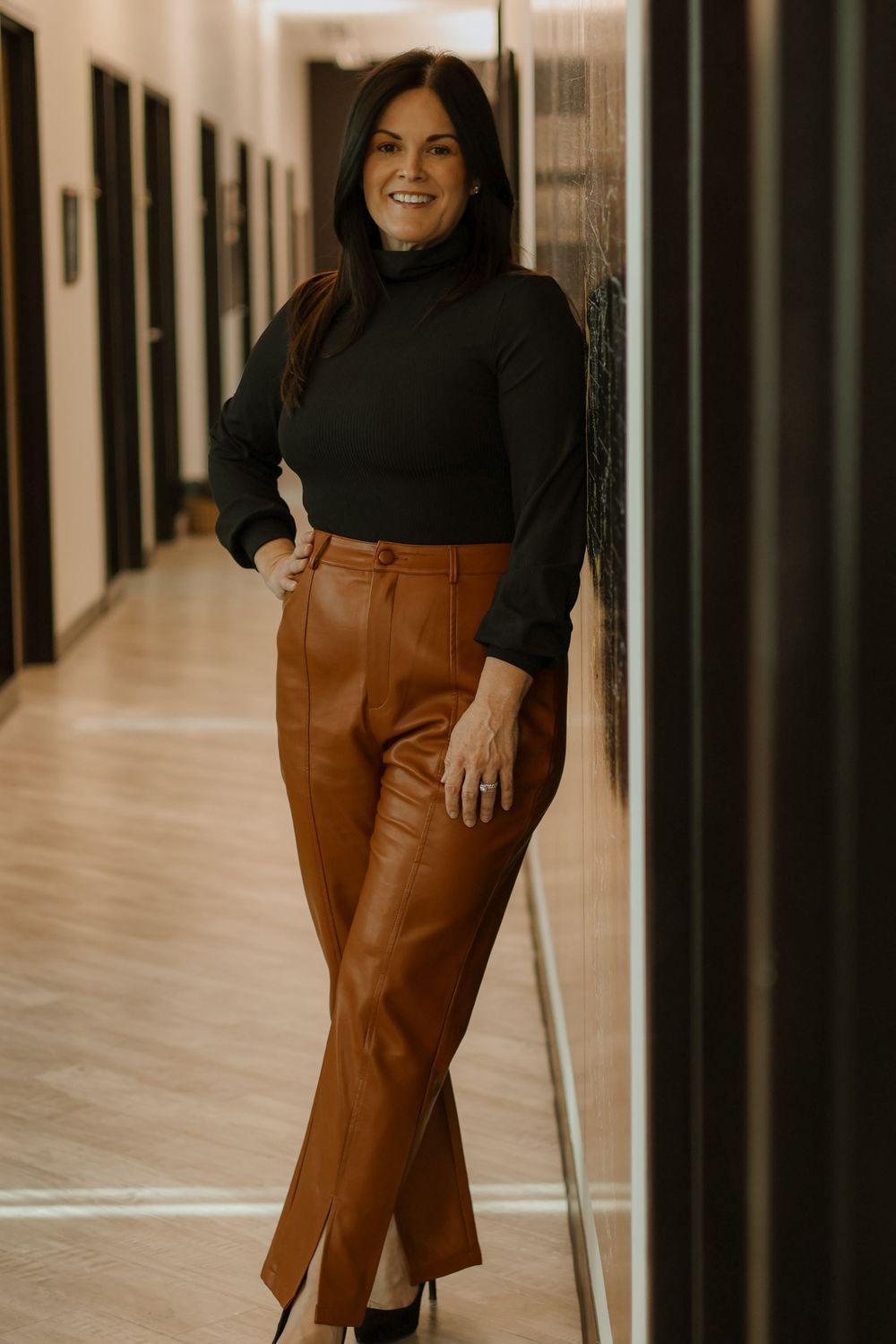 Fashion portraits showing brown leather pants and black top styled in office setting.