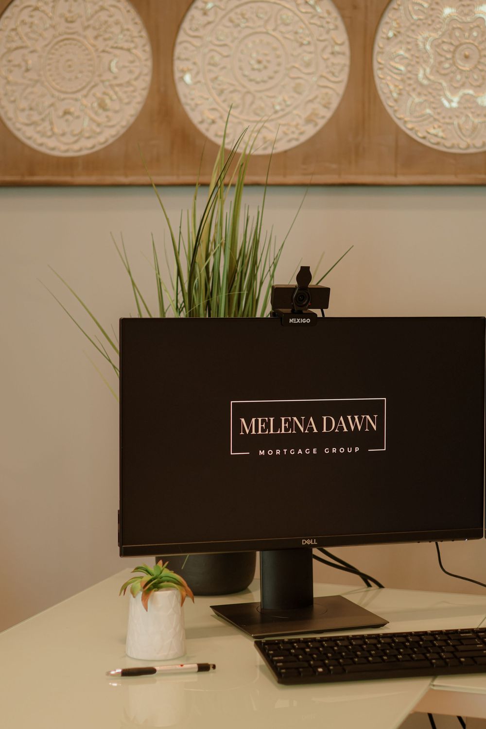 Modern office desk with Melena Dawn branding on monitor and decorative wall art.