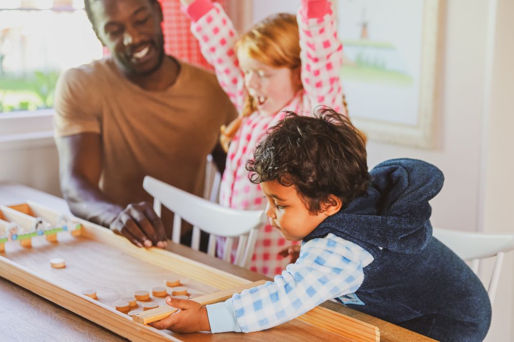 Family enjoying activity time together at table with child in checkered pajamas.