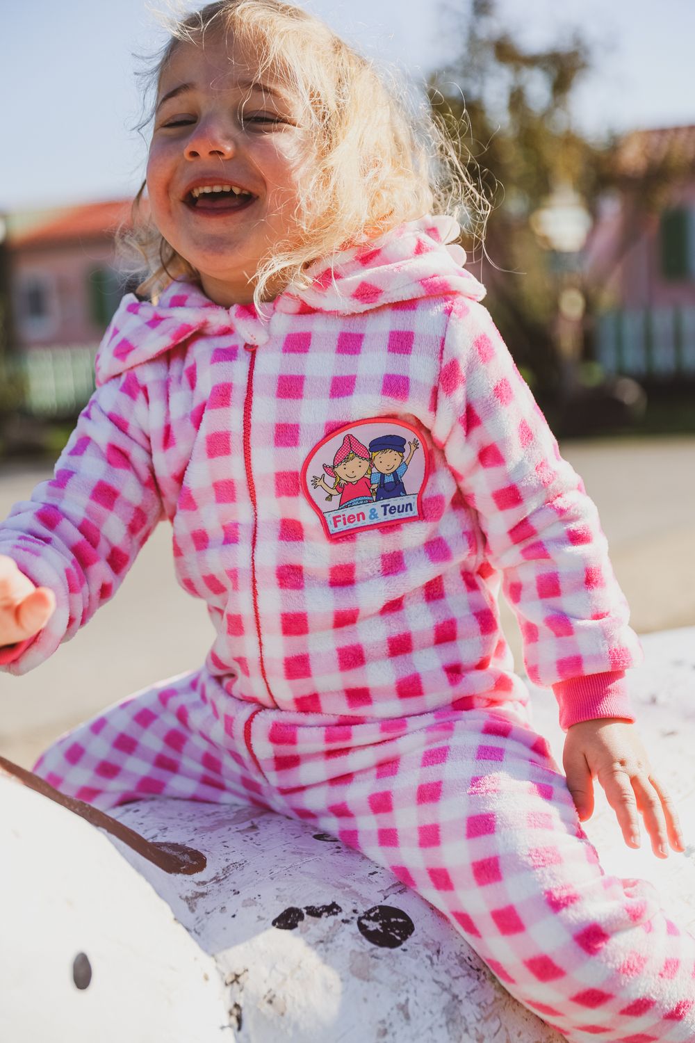 Child wearing pink and white checkered pajamas sitting outdoors on sunny day.